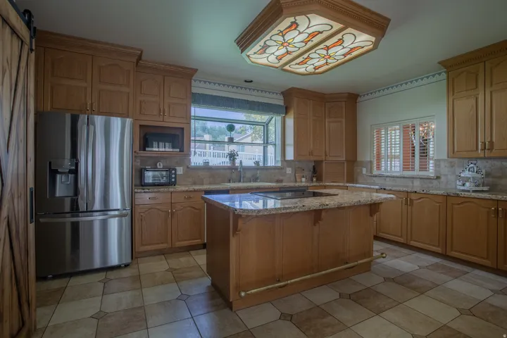 Kitchen featuring wood cabinetry, granite countertops, a central island with cooktop, and tile flooring