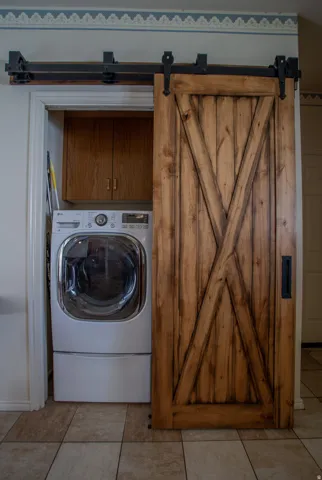 Laundry area featuring a wood barn door, black metal sliding hardware, wood-finish cabinetry, and tiled flooring