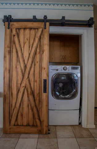 Barn door entry with exposed black hardware, leading to a utility closet with wood-finish cabinetry