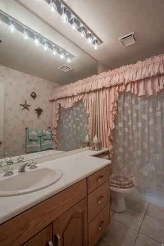 Vanity with an integrated sink and light wood-finish cabinetry, track lighting, and tile flooring
