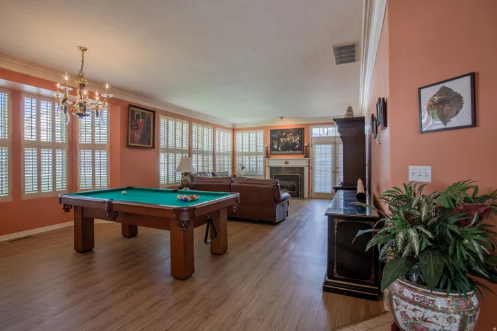 Spacious living area featuring wood-finish flooring, extensive window shutters, a decorative chandelier, and a fireplace with a mantel
