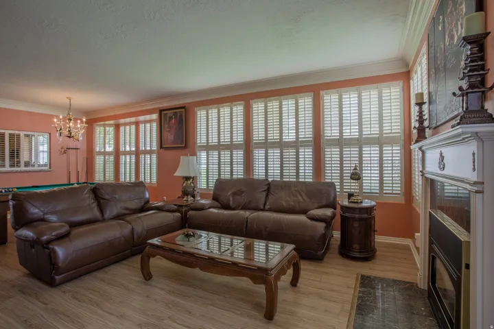 Recessed fireplace with white mantel, wood-finish flooring, multiple windows with plantation shutters, and crown molding