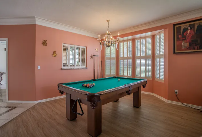 Wood-finish flooring, crown molding, and a bay window featuring plantation shutters