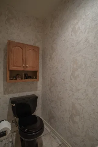 Wood-finish wall cabinet, black toilet, and tiled flooring