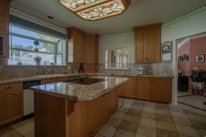 Kitchen featuring wood cabinetry, granite-finish countertops, a built-in stovetop, a tile backsplash, and patterned floor tiling