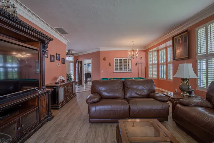 Wood-finish flooring throughout, crown molding detailing, multiple windows with plantation shutters, and a chandelier light fixture