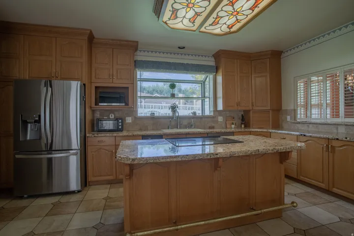 Wood-finish cabinetry with crown molding, granite countertops, tile flooring, stainless steel refrigerator, and a stained-glass ceiling fixture