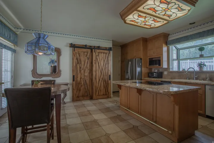 Kitchen featuring a center island with integrated cooktop, wood cabinetry, stainless steel appliances, and a tiled floor