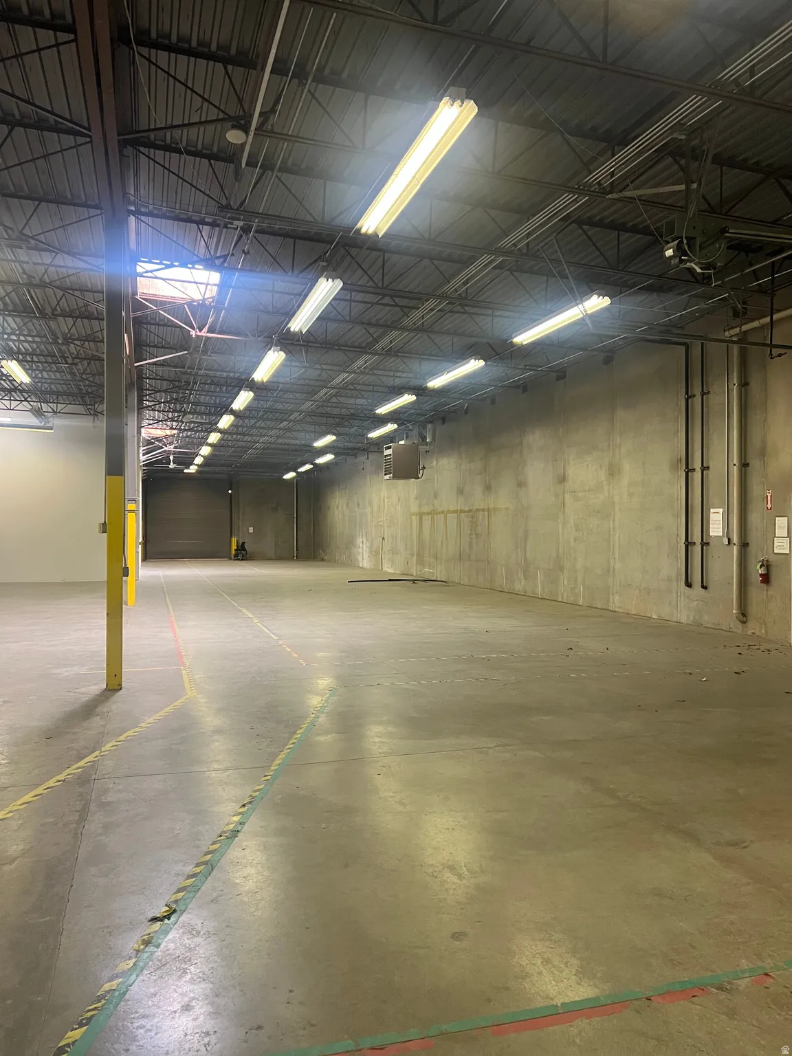 Expansive concrete flooring in a large open-plan area with exposed ceiling trusses and abundant fluorescent lighting