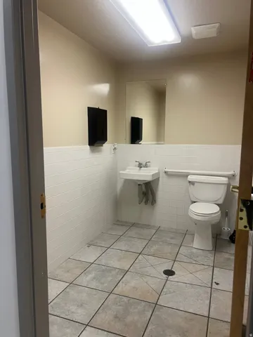 White subway tile wainscoting, wall-mounted sink, ceramic commode, and tiled flooring
