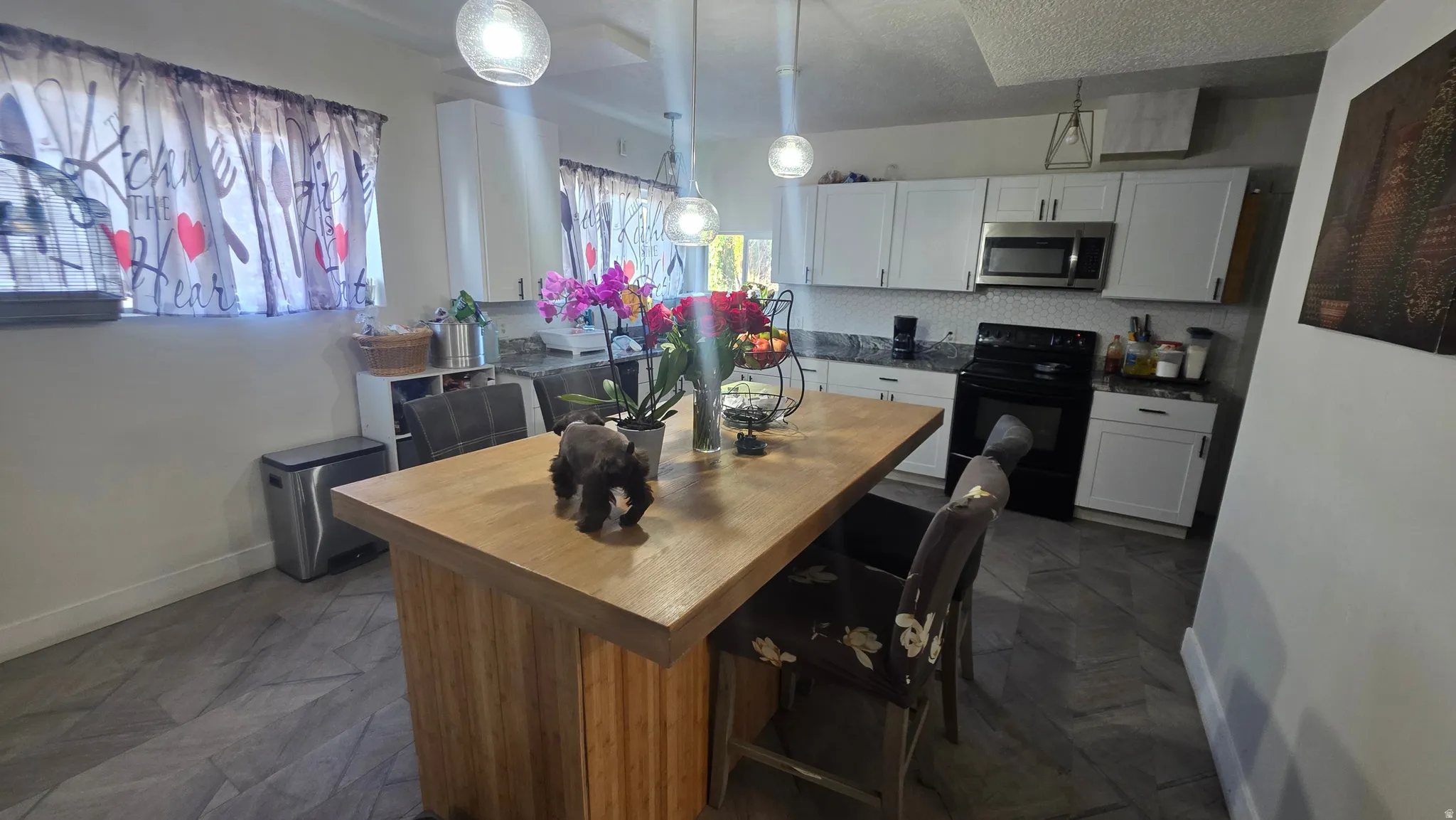 Kitchen featuring white cabinetry, dark countertops, a tiled backsplash, stainless steel microwave, and an island with a wood-finish top
