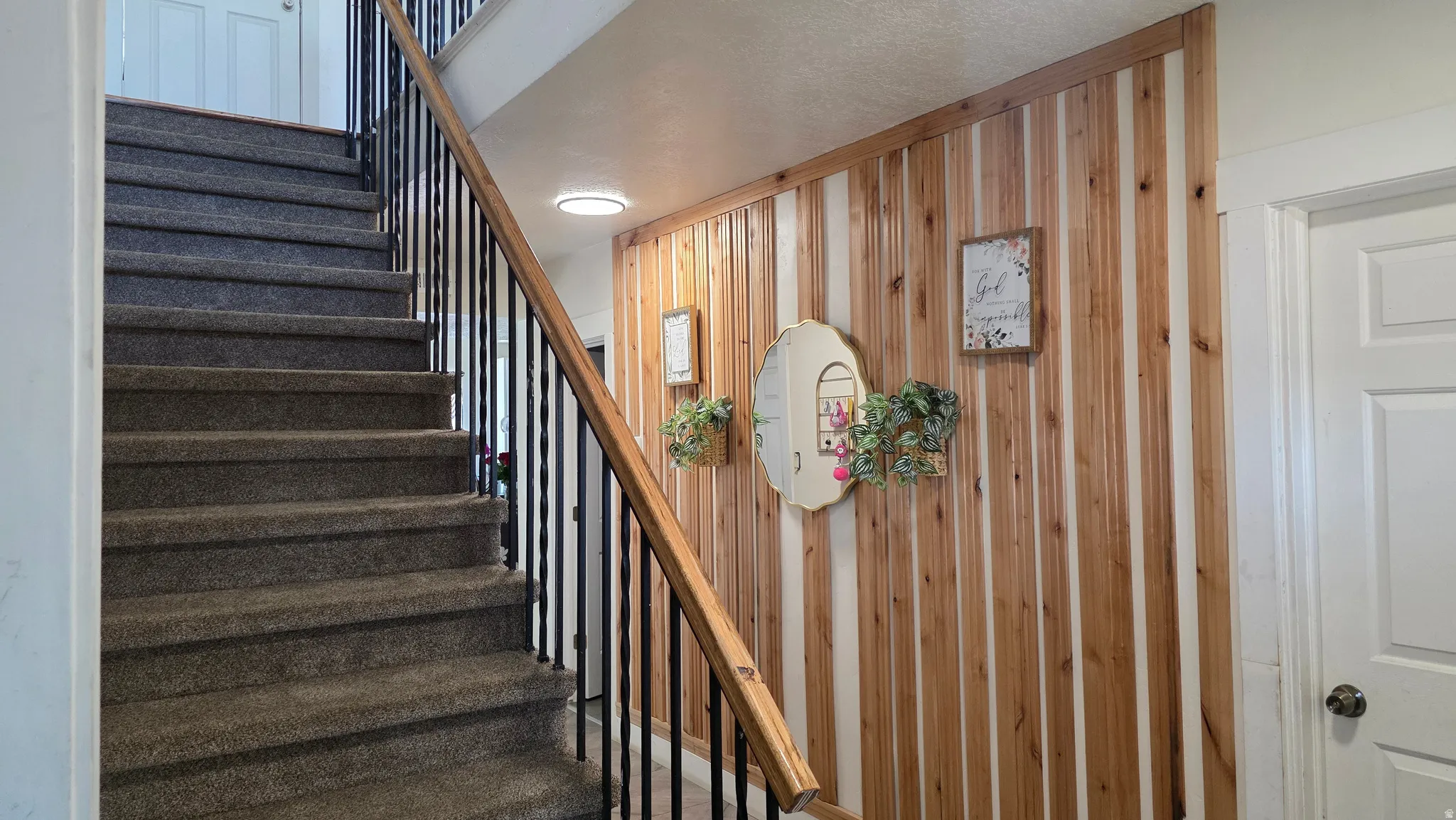 Carpeted staircase featuring a black metal spindle railing with a wood-finish handrail, complemented by a wood-finish accent wall