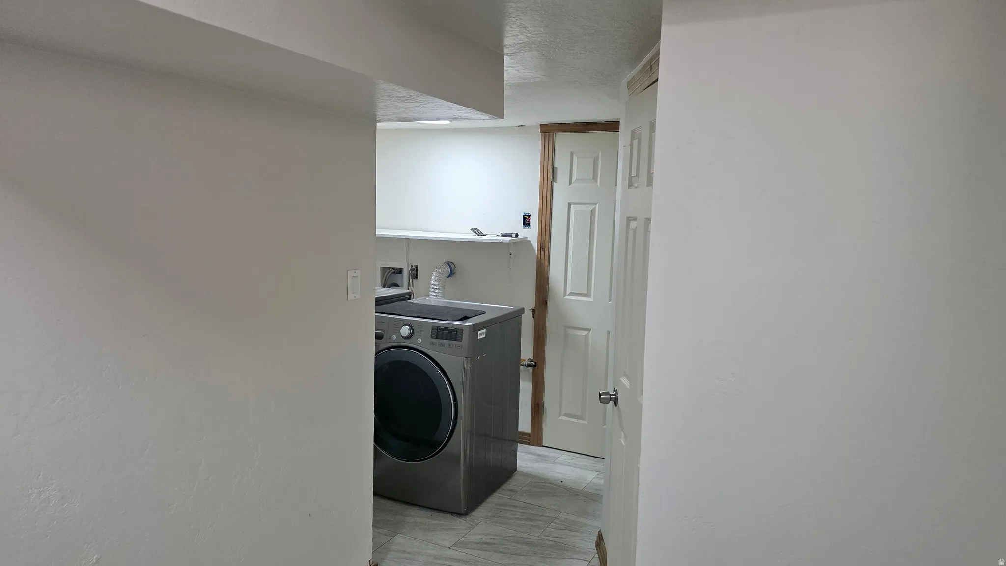 Laundry area featuring a built-in shelf, white paneled door, and light-toned flooring