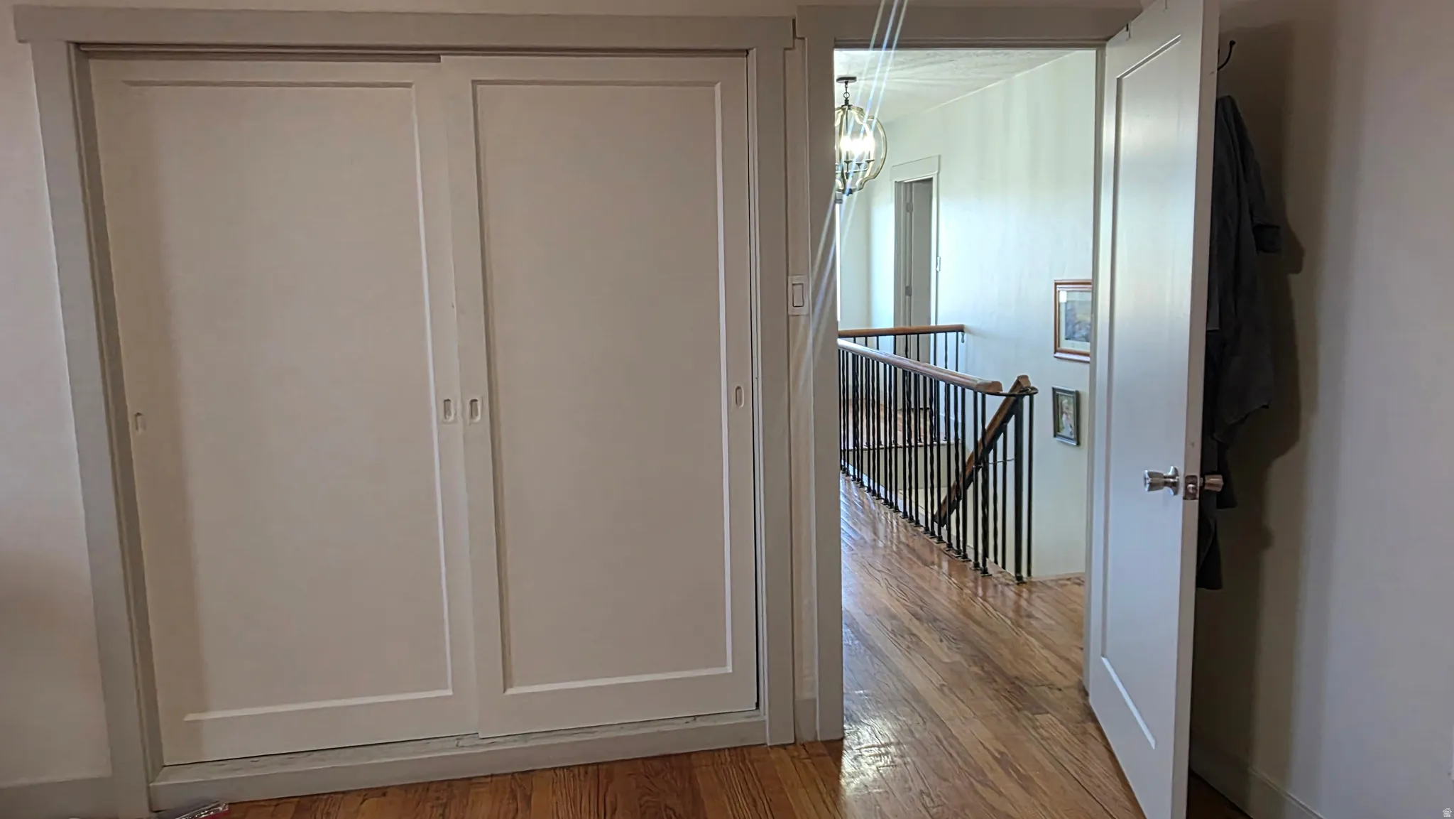 White sliding closet doors, wood-finish flooring, white paneled interior door, black metal stair railing, and a decorative ceiling light fixture