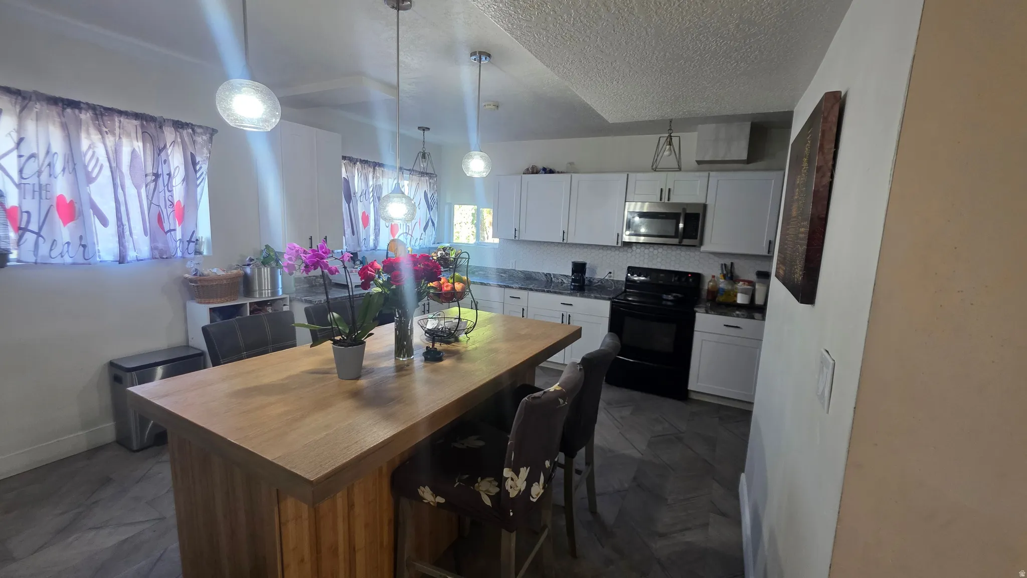 Kitchen featuring wood-finish flooring, white cabinetry, dark countertops, a black appliance suite, and a wood-finish island with pendant lighting