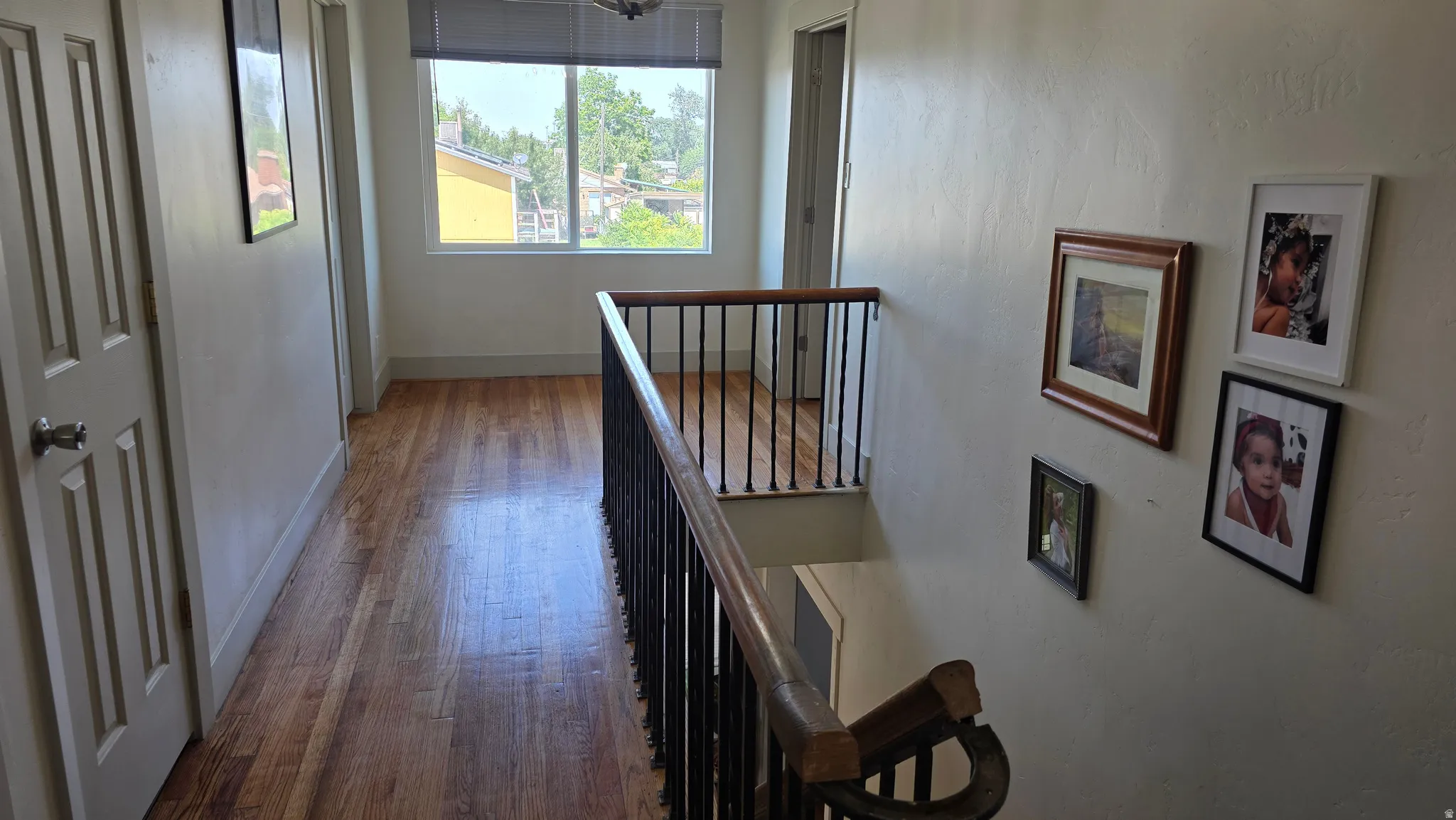 Hardwood flooring throughout, white painted walls, white trim, and a window with a roller shade