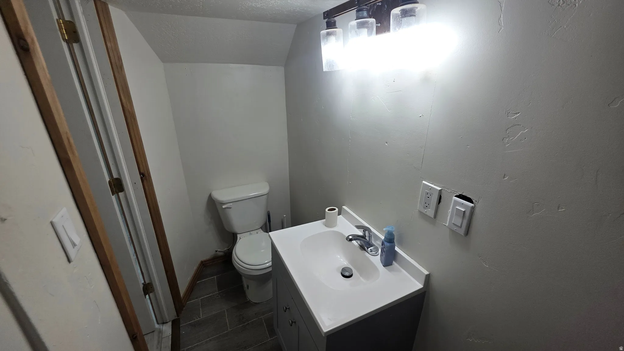 Recessed ceiling, wood-finish door frame, white toilet, vanity with integrated sink, and a three-light fixture