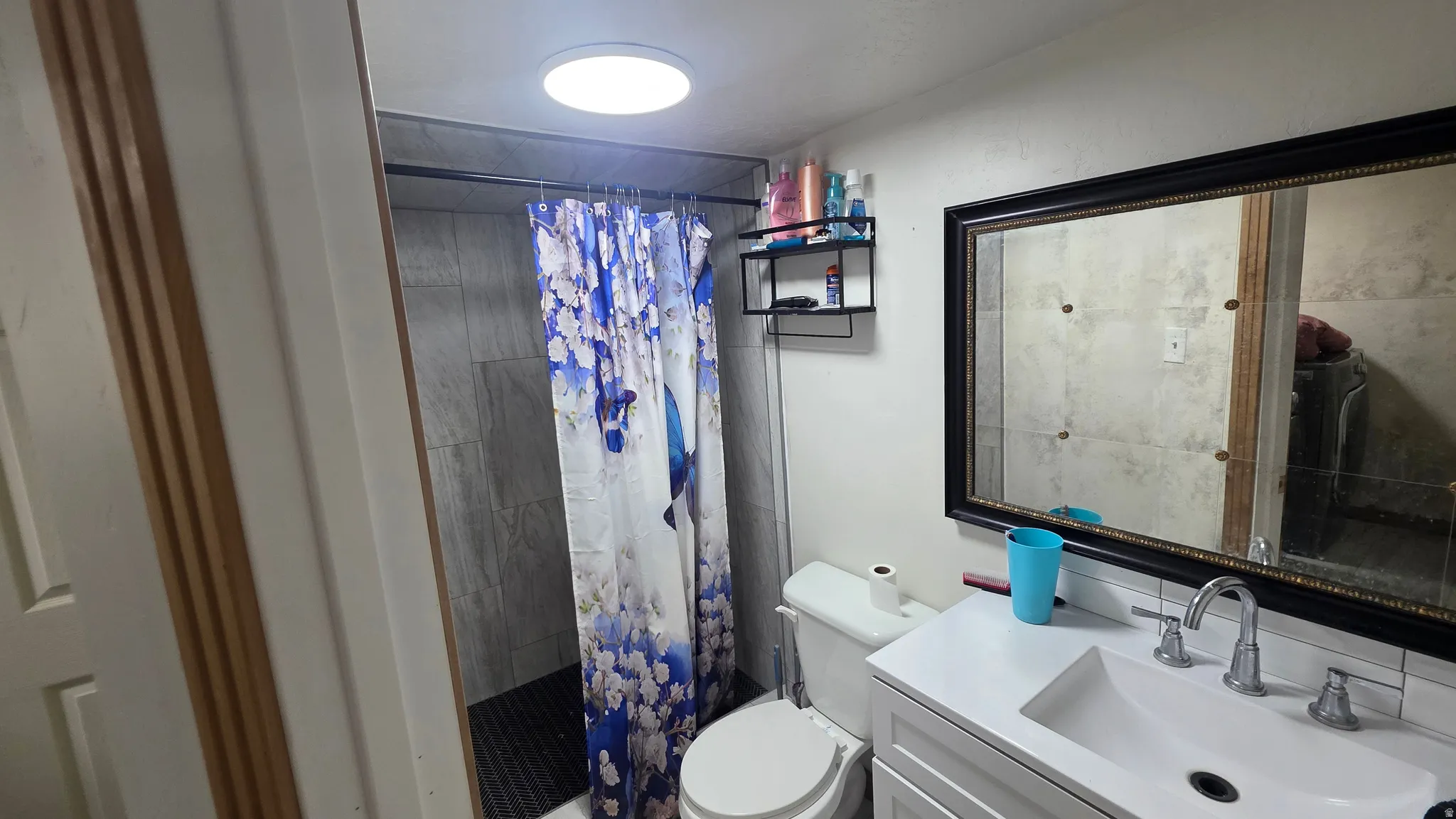 Recessed ceiling light, vanity with integrated sink, framed mirror, and tiled shower surround
