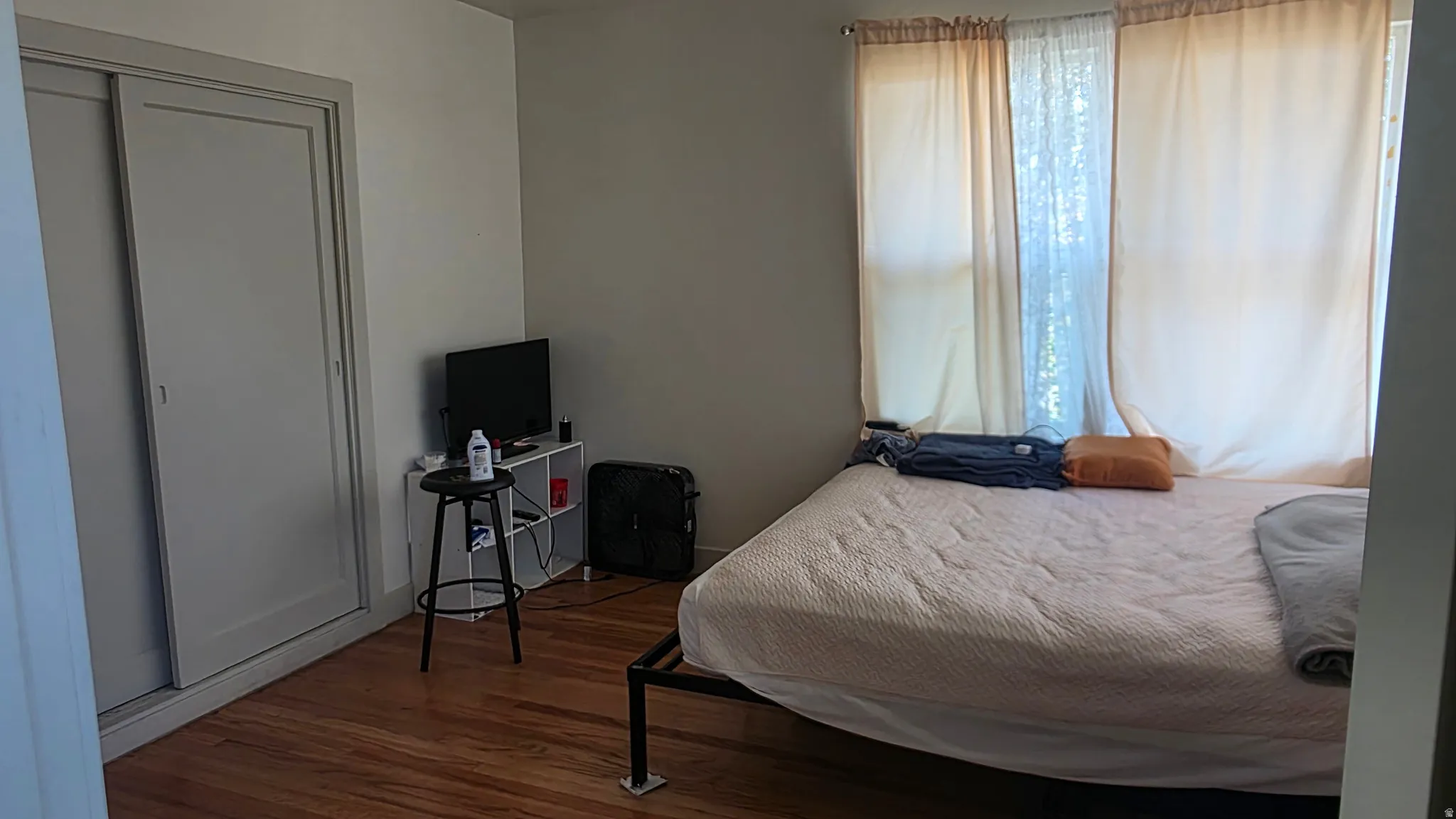 Wood-finish flooring with a light gray wall color, two windows with light-filtering curtains, and a sliding door closet
