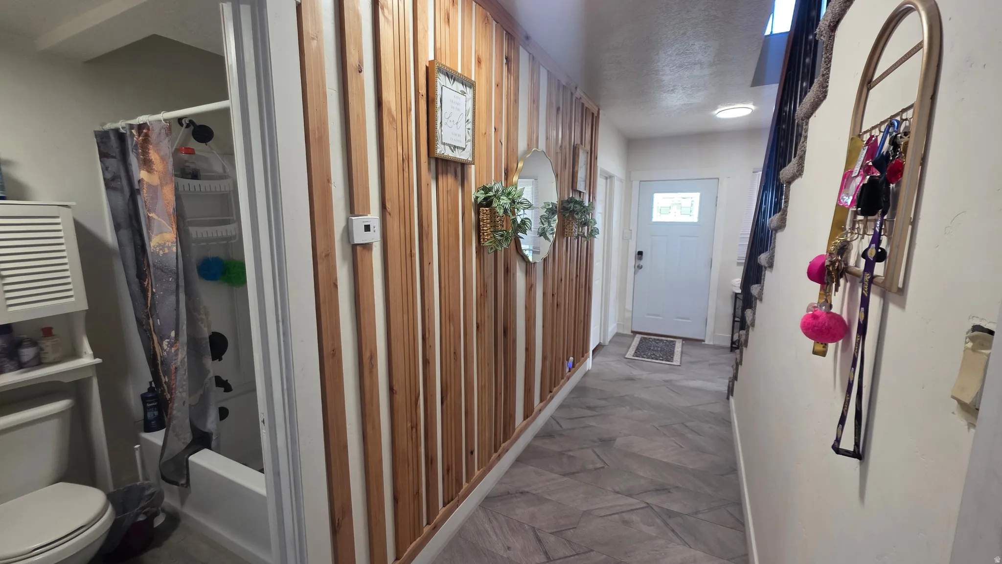 Wood-paneled accent wall, tiled flooring, built-in bathtub with shower, white paneled door, and staircase with dark railing