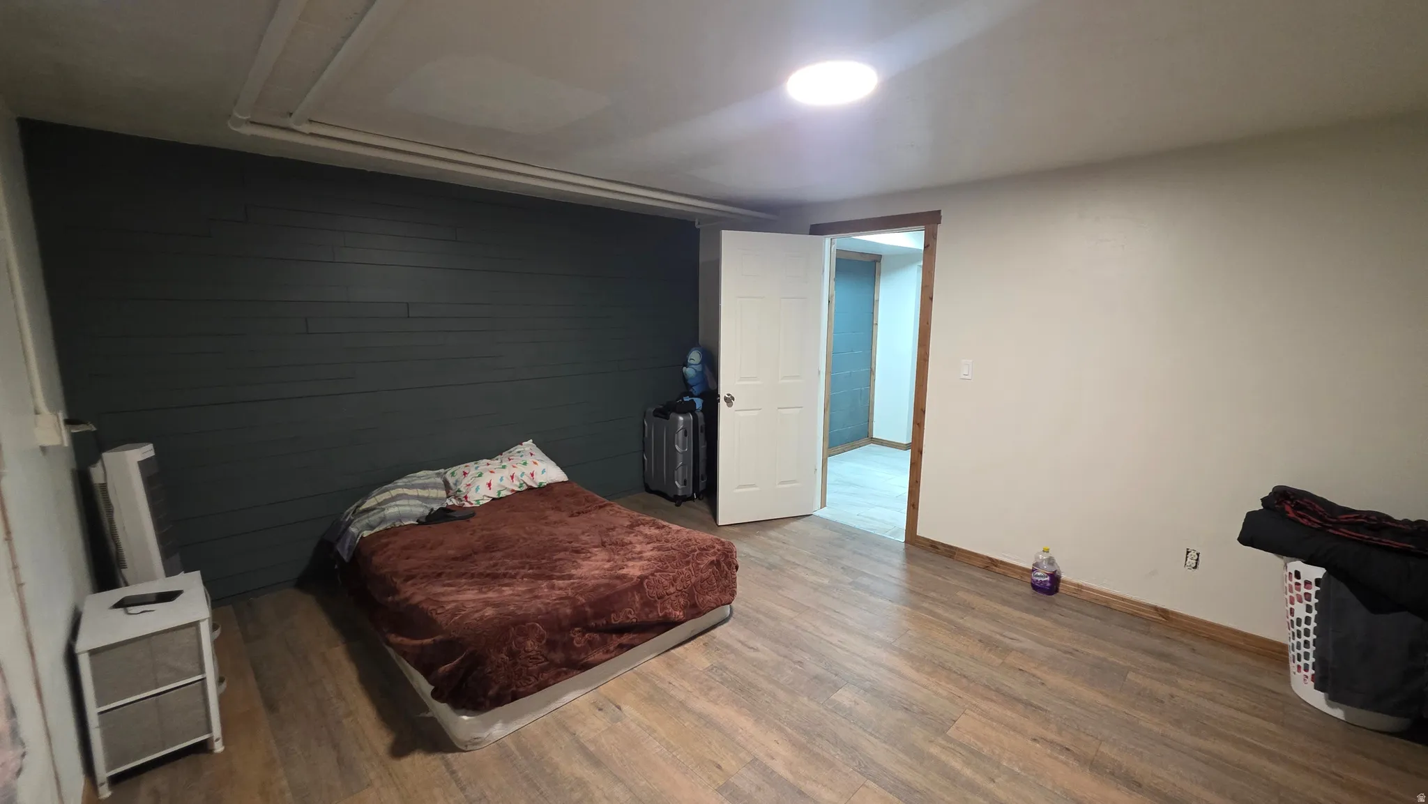 Spacious bedroom with wood-finish flooring, accent wall with horizontal shiplap detailing, and abundant natural light from recessed ceiling fixtures