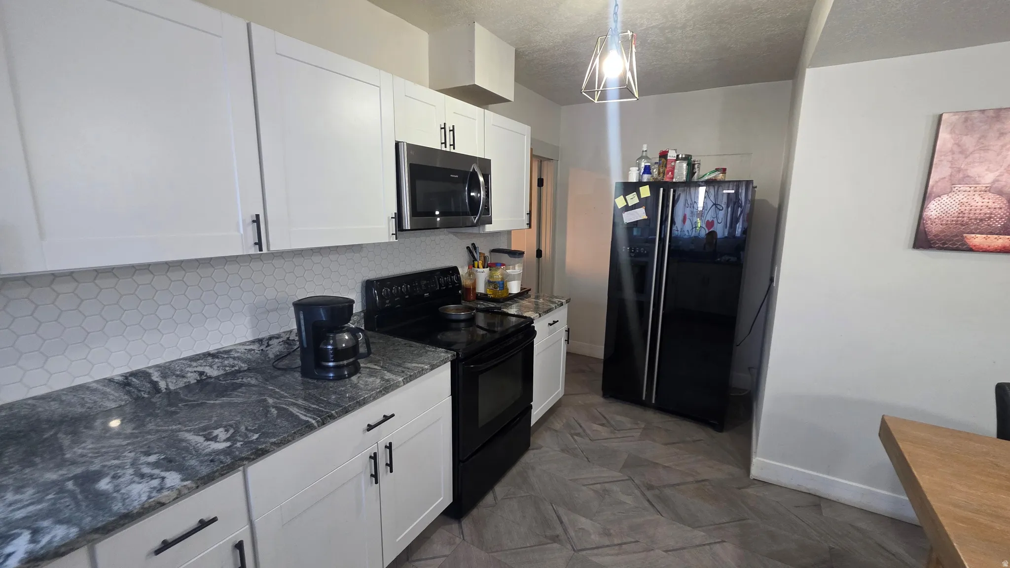 White shaker-style cabinetry with matte black hardware, hexagonal tile backsplash, marbled countertops, and large format chevron tile flooring