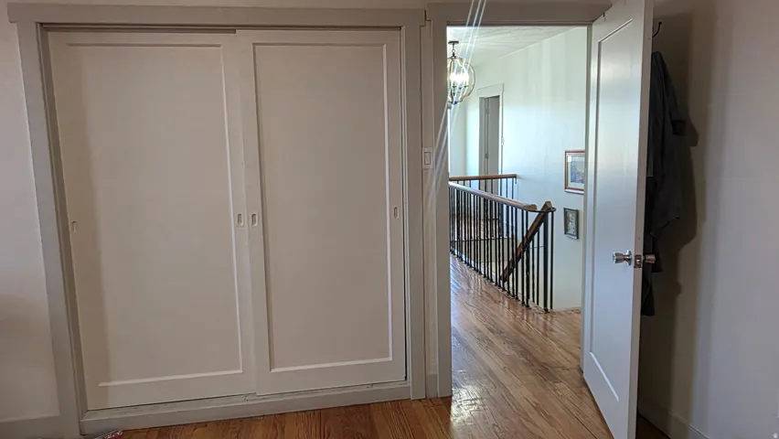 White sliding closet doors, wood-finish flooring, white paneled interior door, black metal stair railing, and a decorative ceiling light fixture