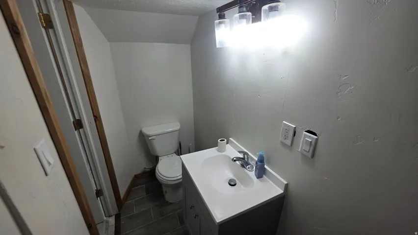 Recessed ceiling, wood-finish door frame, white toilet, vanity with integrated sink, and a three-light fixture