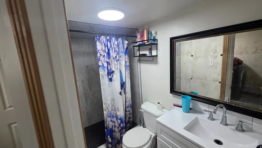 Recessed ceiling light, vanity with integrated sink, framed mirror, and tiled shower surround