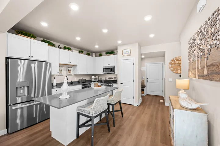Kitchen featuring white cabinetry, stainless steel appliances, a center island with a stone countertop, and wood-finish flooring