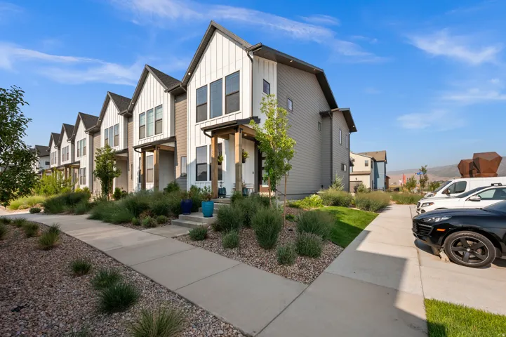 Modern multi-level townhome featuring vertical white siding, gray horizontal siding, an angled roofline, and a covered entry with wood-finish columns