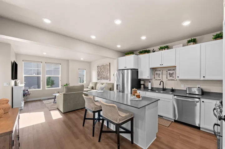 Open-concept living space featuring wood-finish flooring, recessed lighting, white cabinetry, stainless steel appliances, and a kitchen island with seating