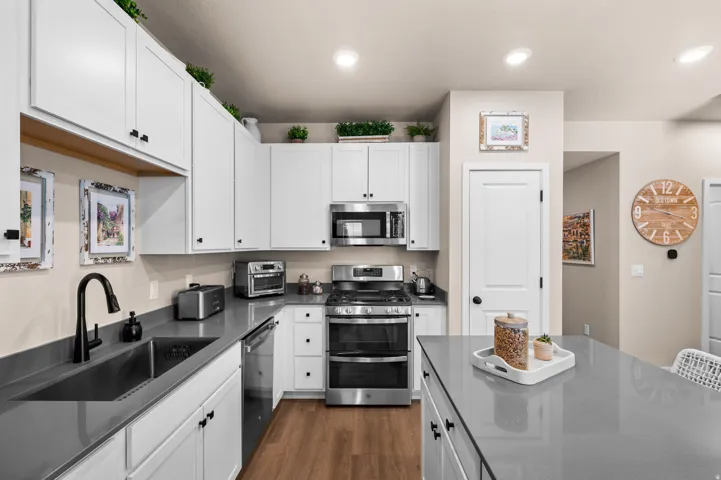 White cabinetry, stainless steel appliances, recessed lighting, wood-finish flooring, and a kitchen island with a stone-finish countertop
