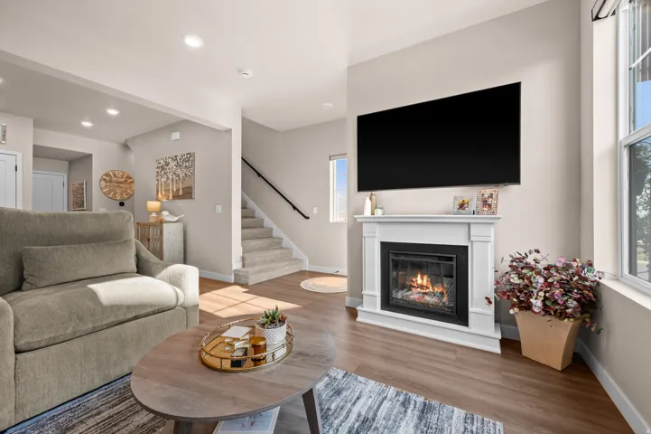 Living area featuring a white mantel fireplace, wood-finish flooring, recessed lighting, and a staircase with carpeted treads