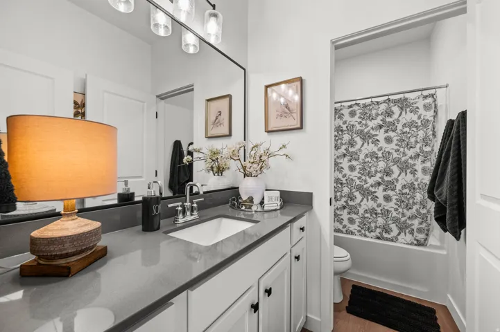 Single vanity with an integrated sink and gray countertop, white cabinetry with black hardware, and an elongated mirror with a multi-bulb light fixture