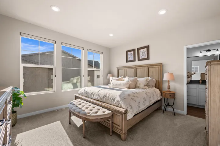 Recessed ceiling lighting, three paneled windows, carpeted flooring, and an adjoining bathroom with a vanity featuring a dark countertop and a wall-mounted light fixture