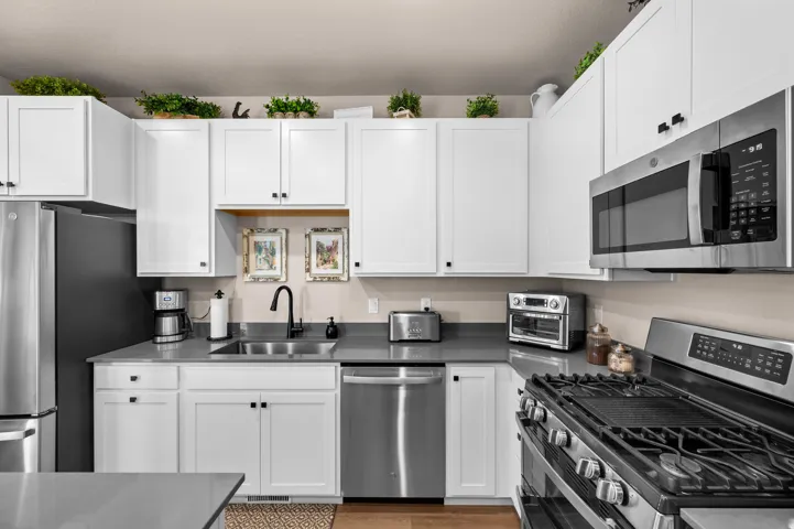 White upper and lower cabinetry, stainless steel appliances, dark countertop, dual basin sink with a matte black faucet, and a gas range