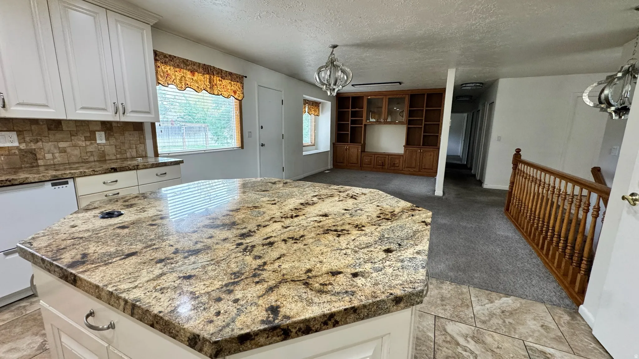 Spacious kitchen island with stone countertop, white cabinetry, tile flooring, and integrated built-in shelving