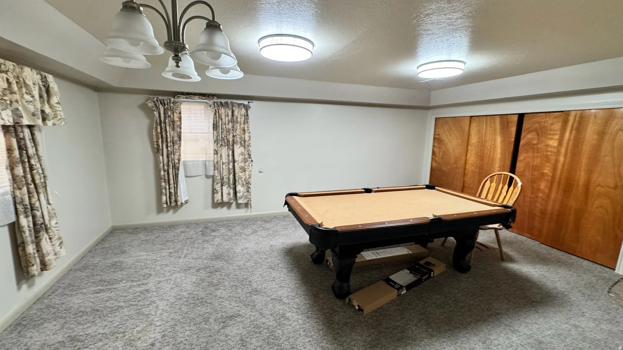 Carpeted interior space featuring a multi-light chandelier, two flush-mount ceiling lights, and two windows with blinds