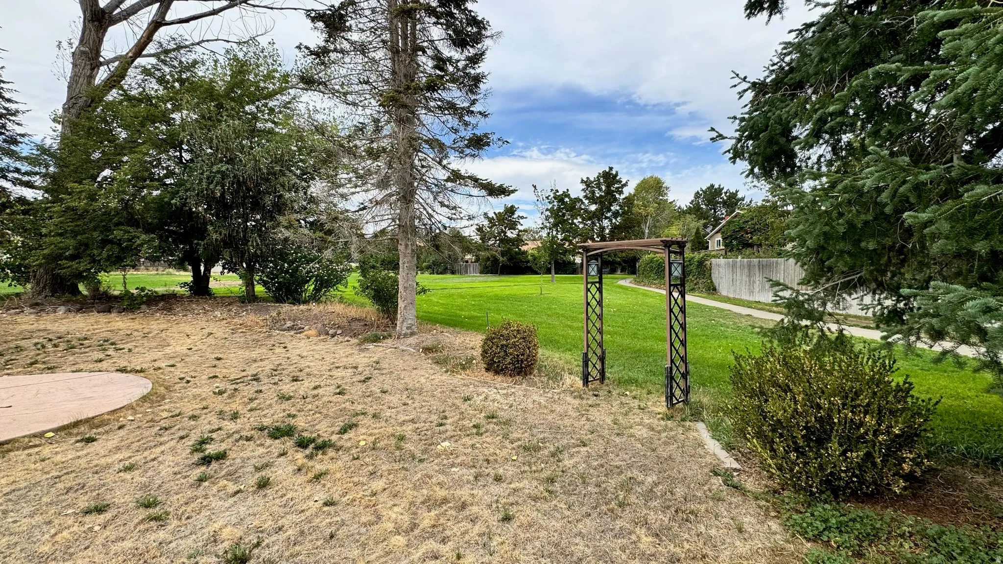 Expansive green space with mature trees, a decorative metal archway, and a concrete pathway