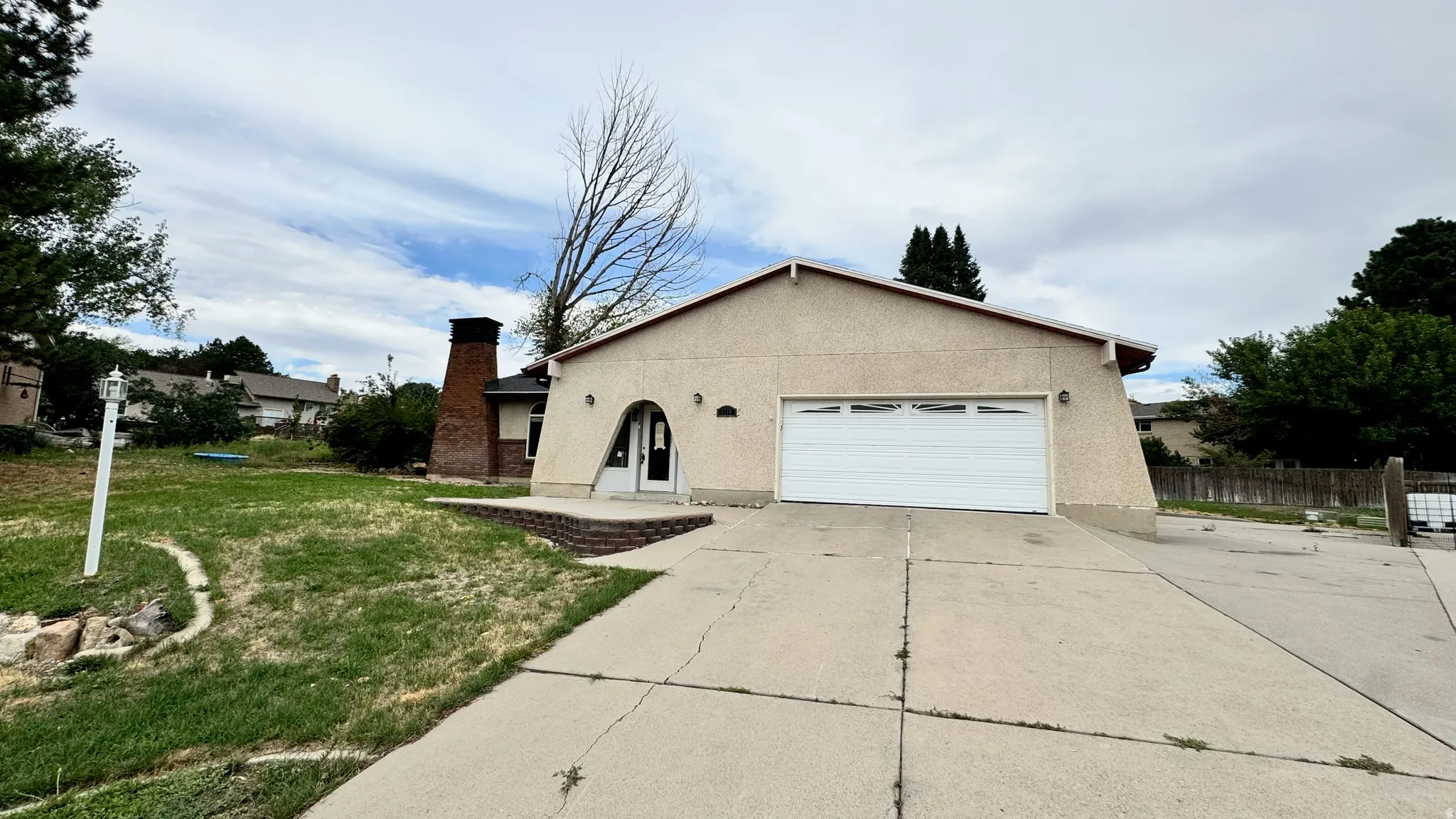 Stucco exterior with a two-car garage, concrete driveway, and brick chimney