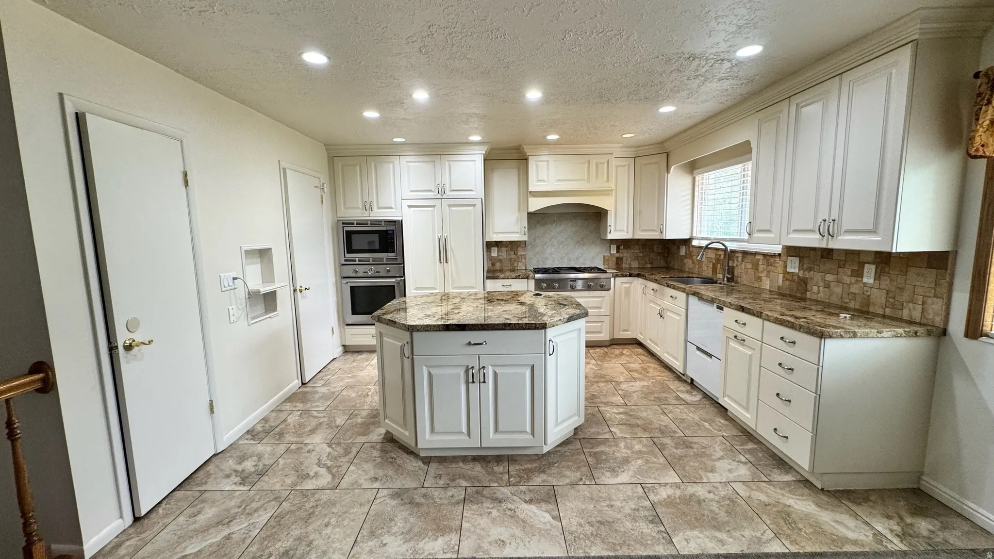Kitchen featuring an octagonal island, white cabinetry, integrated stainless steel appliances, tile flooring, and a tiled backsplash