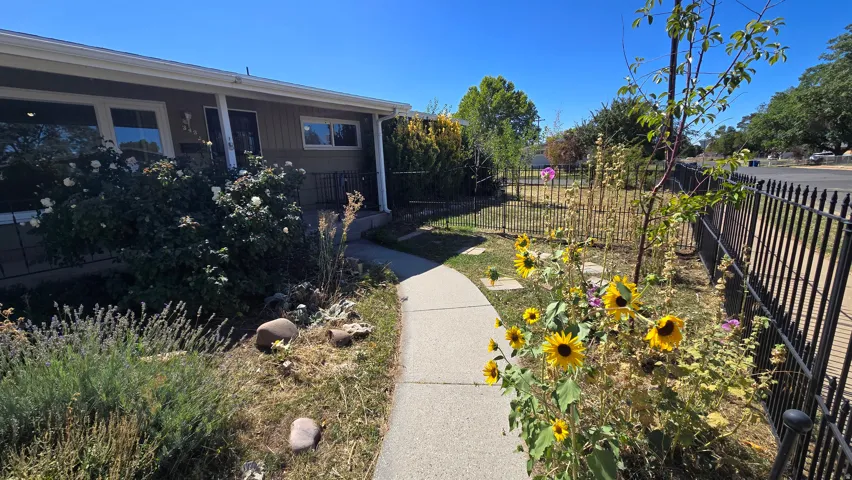 Front exterior with a concrete walkway, mature shrubs, a decorative metal fence, and a landscaped garden area
