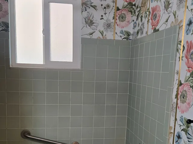Bathroom with light green tiled walls, a green bathtub, and a window with frosted panes