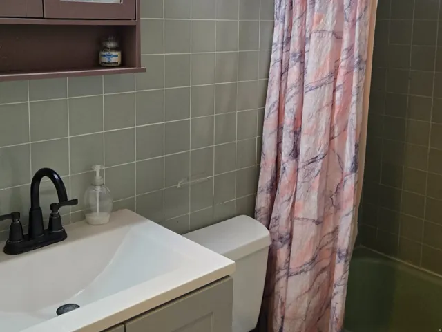 Wall-mounted light fixture, floral wallpaper, sage green wall tile, white vanity with integrated sink, and white commode