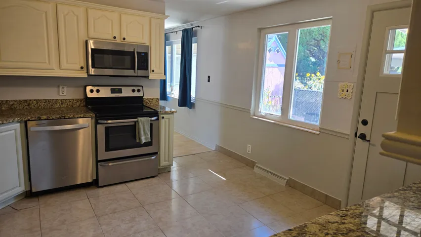 Kitchen featuring light-toned cabinetry, stainless steel appliances, granite-look countertops, and tile flooring