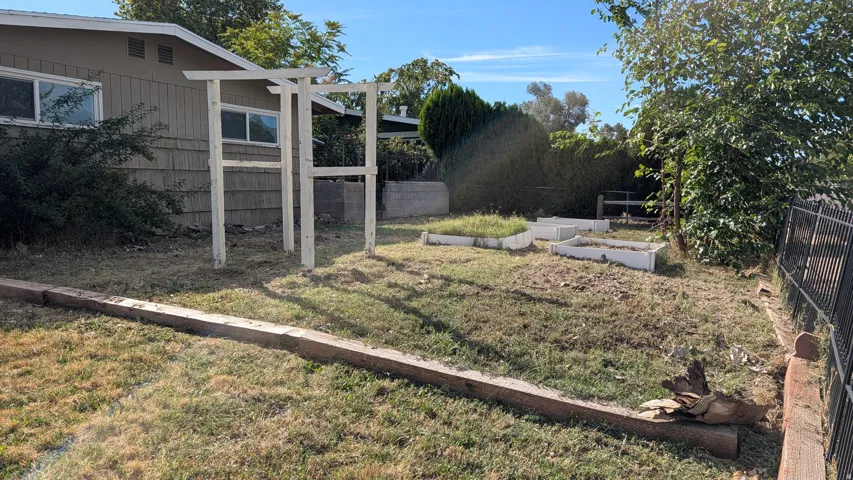 Expansive rear yard featuring raised garden beds, a pergola structure, and perimeter fencing