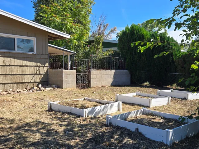 Expansive backyard featuring multiple raised garden beds, mature trees, and a concrete block retaining wall
