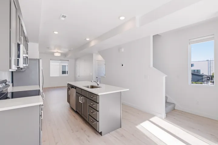 Modern kitchen featuring stainless steel appliances, an island with a sink, light wood-finish flooring, recessed lighting, and a window