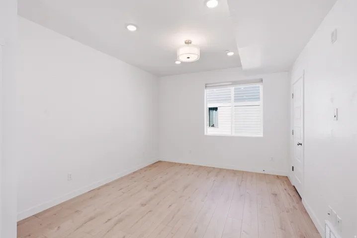 Recessed lighting, wood-finish flooring, central window with blinds, panel door, and flush mount ceiling fixture